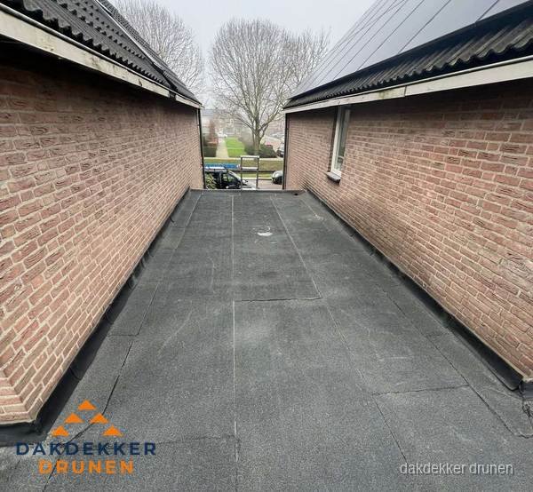 Plat dak met bitumen dakbedekking tussen bakstenen muren in Drunen