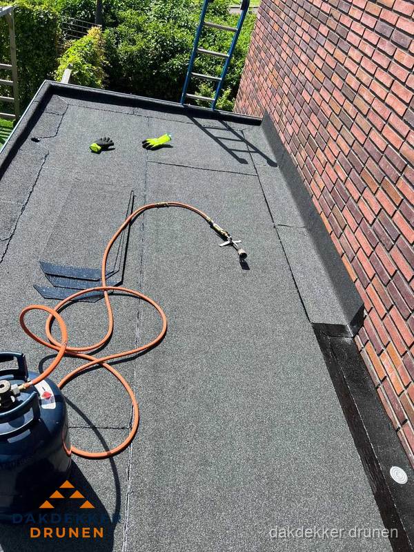 Plat dak met bitumen en brandgereedschap van dakdekkersbedrijf in Drunen